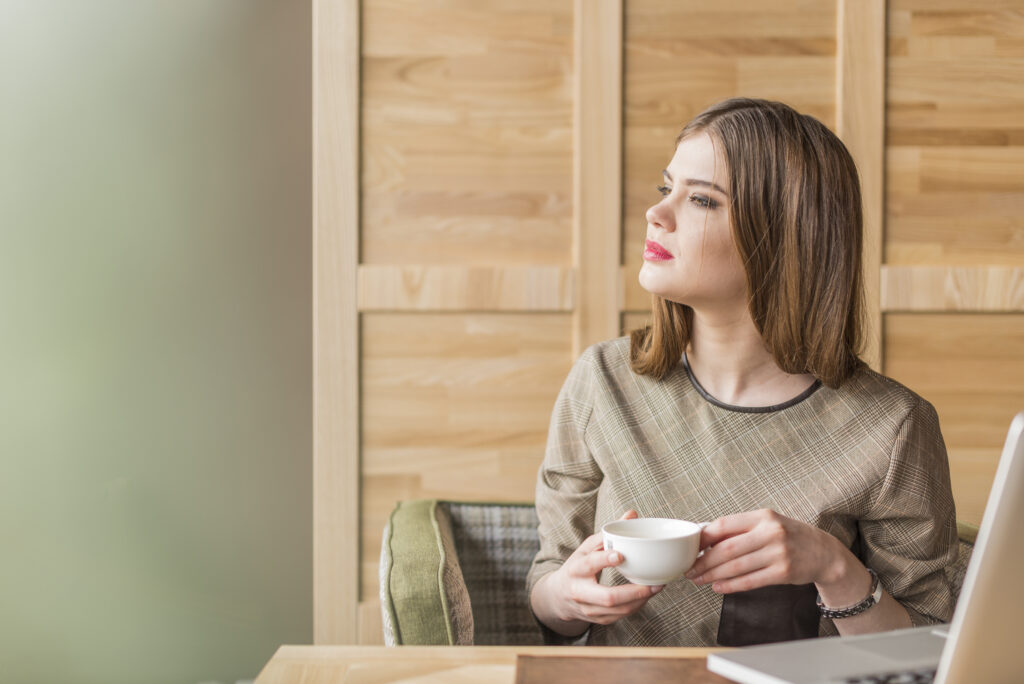 joven contemplando ventana con cafe y compu