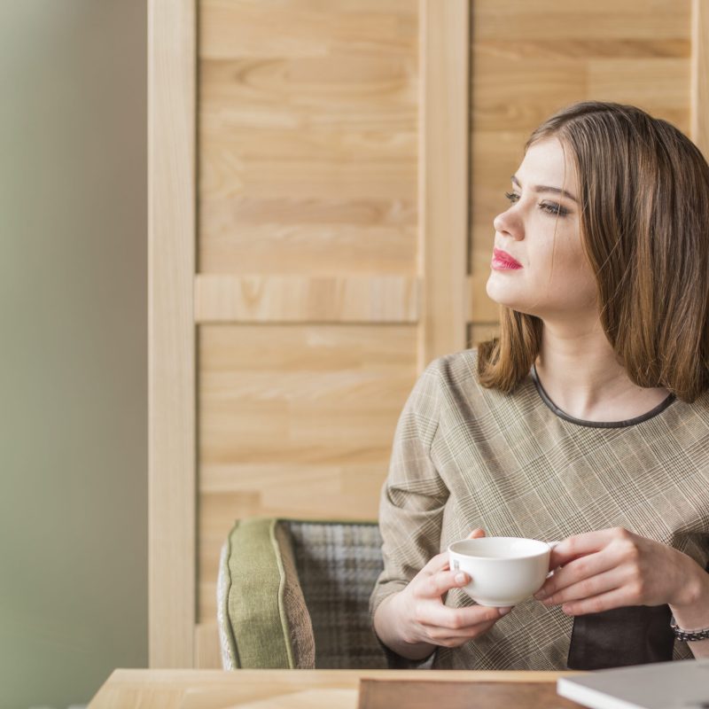 joven contemplando ventana con cafe y compu